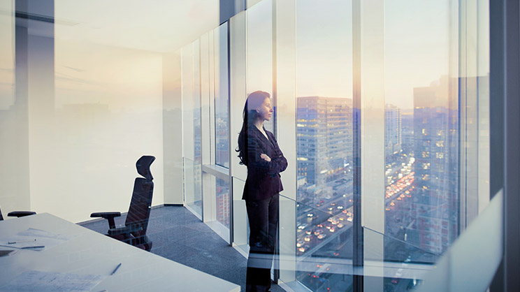 Professional lady observing the outside view through the window glass of skyscraper building 